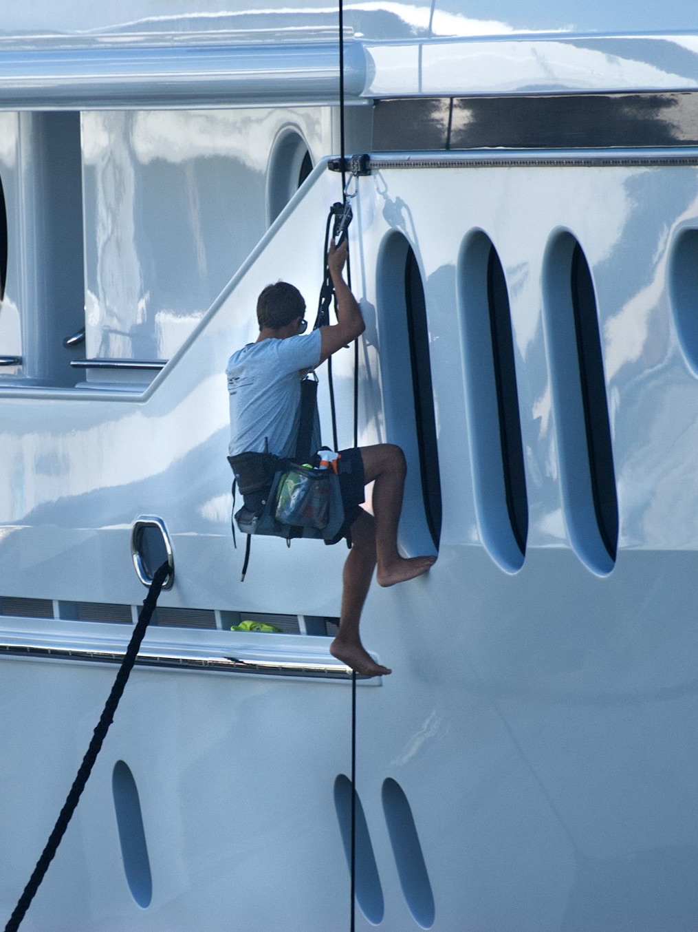A yacht crew member on a rope washing down the hull of a superyacht